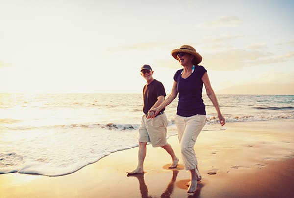 A senior couple walking on the beach while holding hands