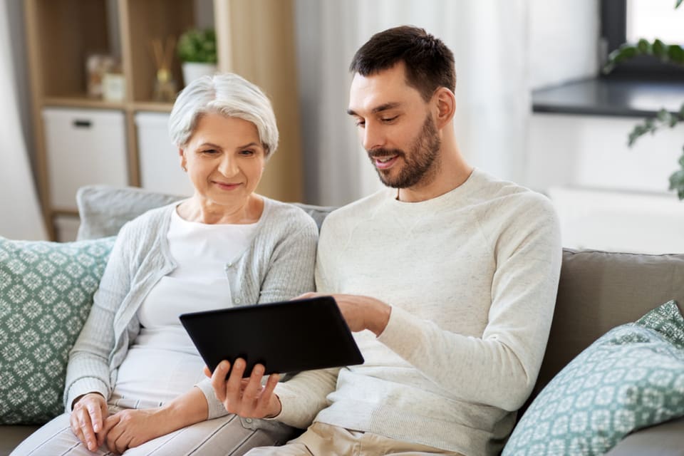 A man and senior woman sit while looking at a digital tablet.