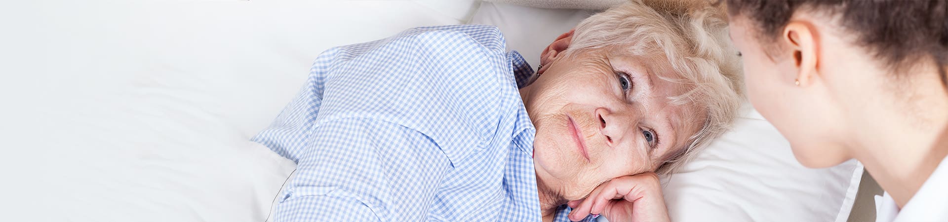 Senior woman resting in bed looking at her caregiver