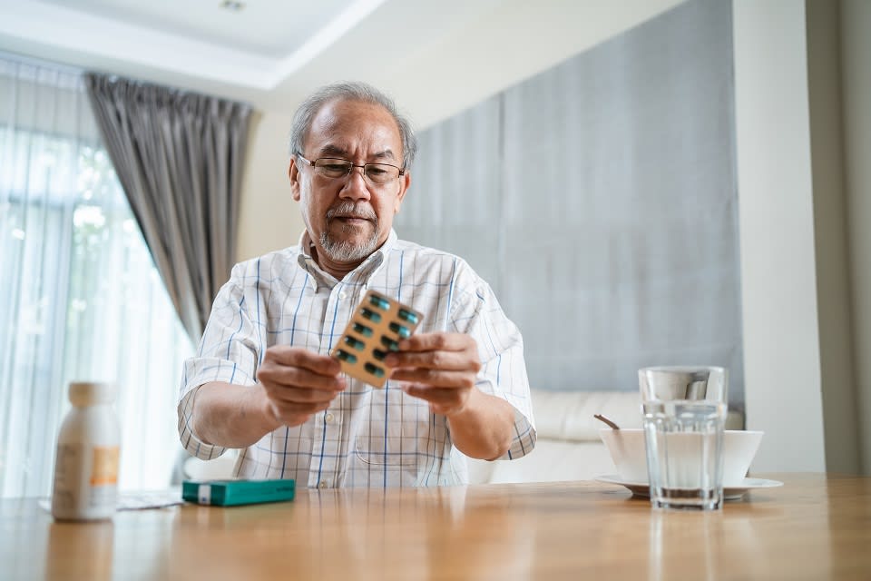 A senior man sits at a table, preparing to take medication.