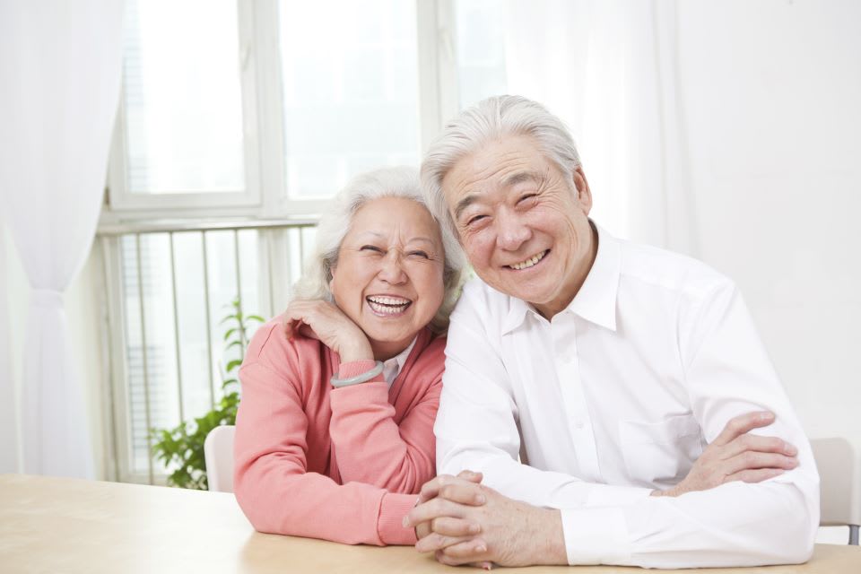 A senior couple sitting on a porch, holding mugs and smiling at each other