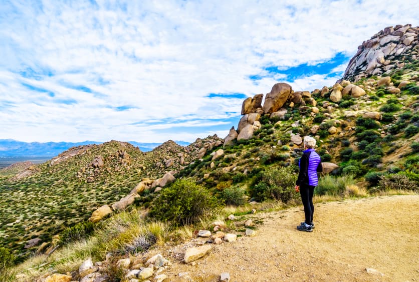 A senior woman standing on a rocky path looking out at the desert