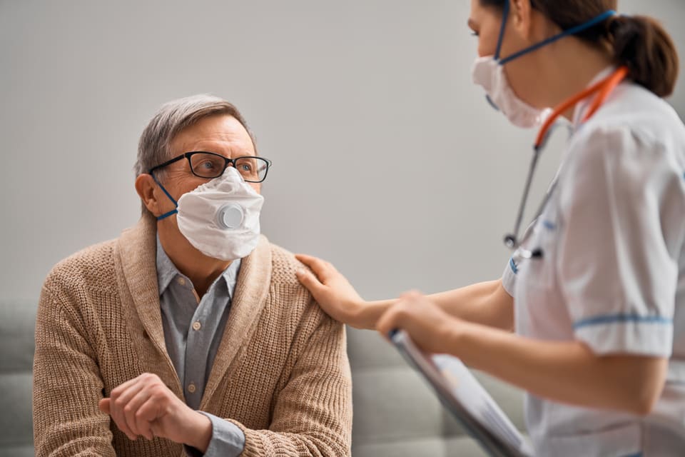A senior man wearing a mask talks to a doctor.