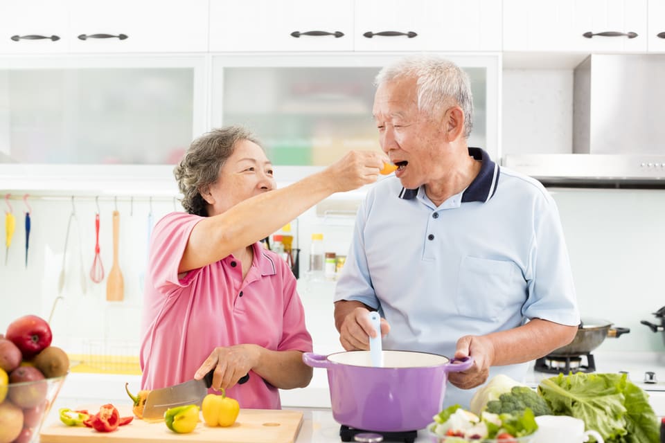 Two seniors try foods while cooking.