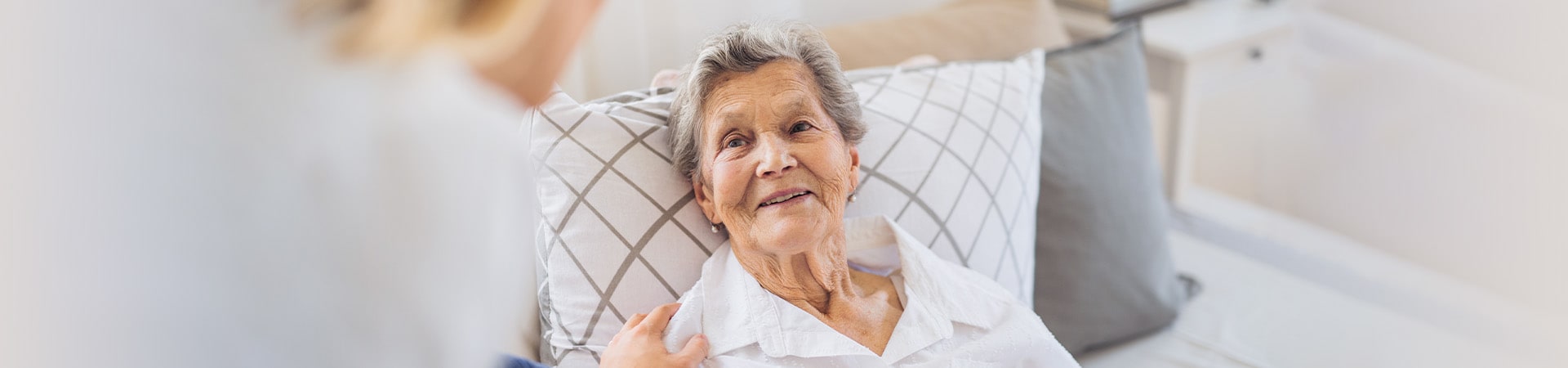 Calm senior looking at caregiver from her bed