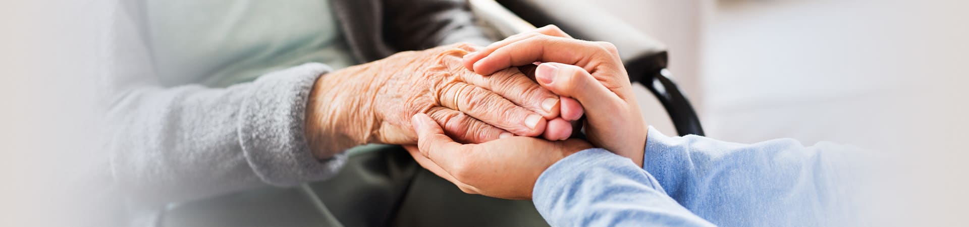 Senior and caregiver delicately holding hands