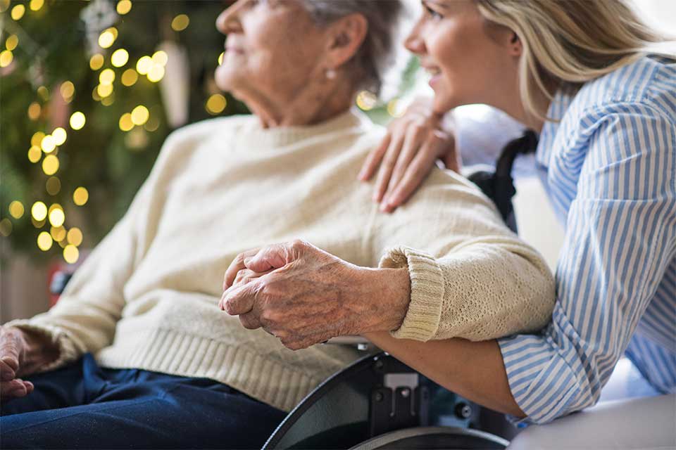 Elderly female in wheelchair holding hands with caregiver.