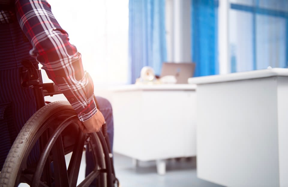 Partial view of man in plaid shirt in wheelchair near white desks