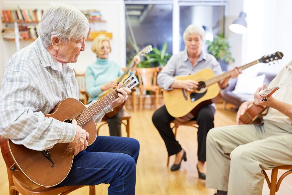 A group of seniors play guitar in a bright room.