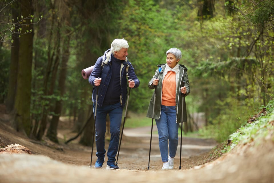 Two seniors hiking in the woods using walking poles.