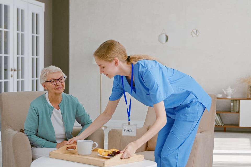 A senior woman is helped by a woman wearing scrubs.