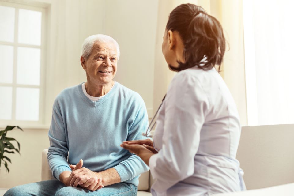 A senior sits in a chair while speaking to a doctor.
