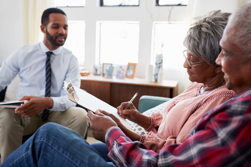 Two seniors sit and take notes while speaking with a man in an office.