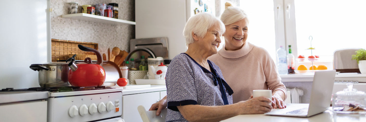 Two senior women smile while looking at a laptop together