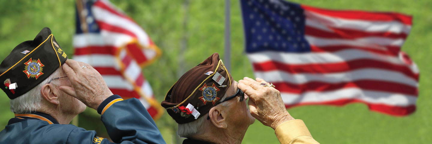 Two senior veterans in uniform saluting American flags