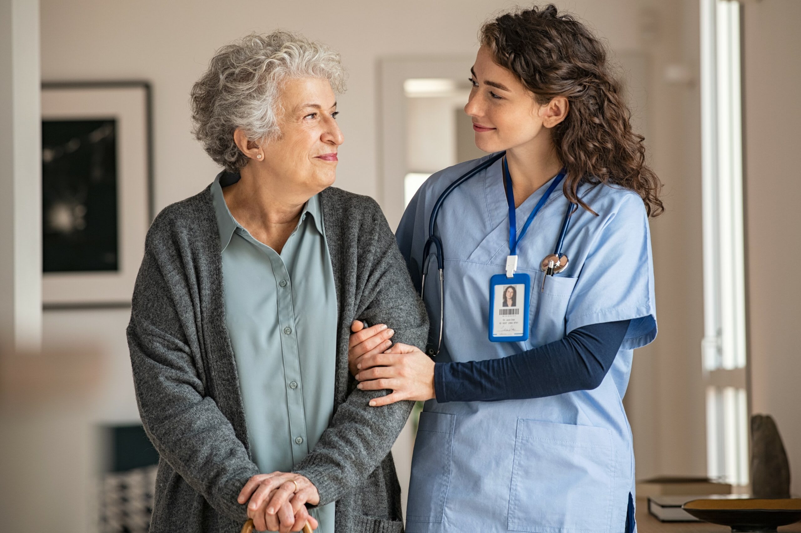 A senior woman walks with a nurse.