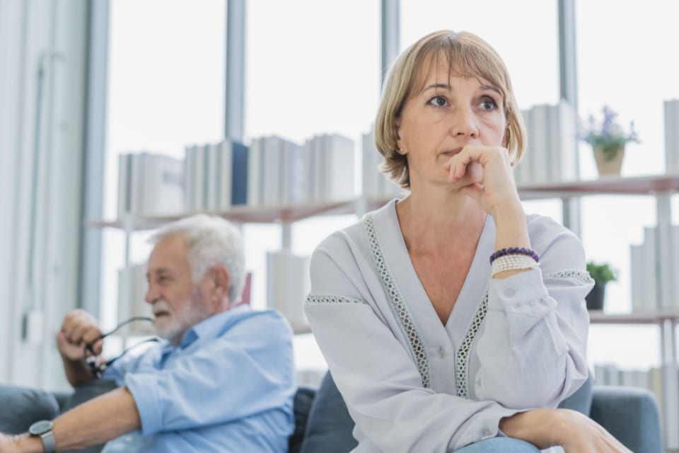 A family caregiver expresses concern while her senior loved one sits in the background