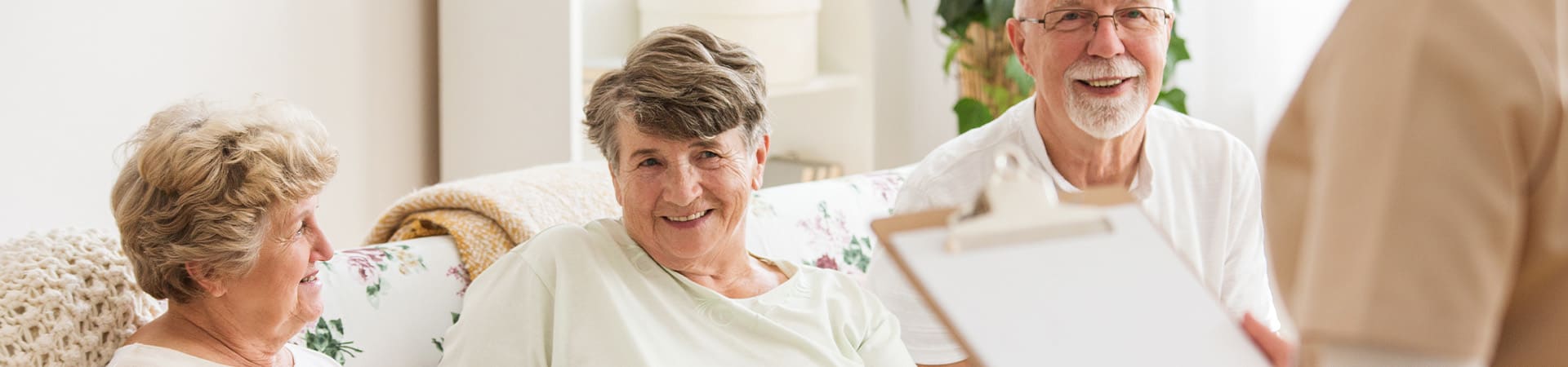 Group of seniors smiling seniors on a couch with a caregiver holding a checklist