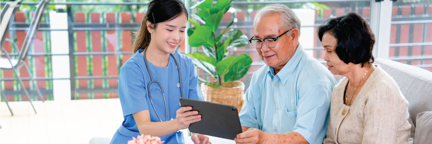 A caregiver smiling and showing a tablet device to a senior couple
