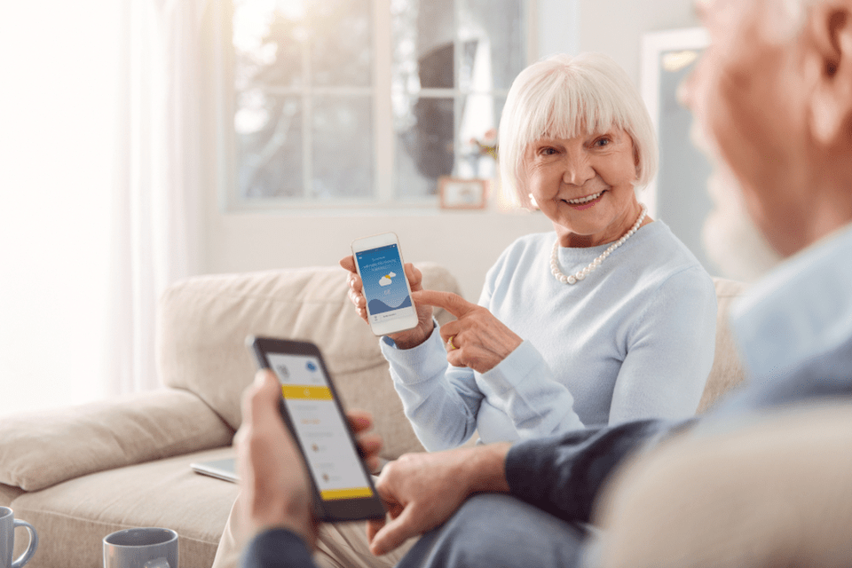 Smiling older woman showing man a picture on her smart phone while he looks at an app on his phone.