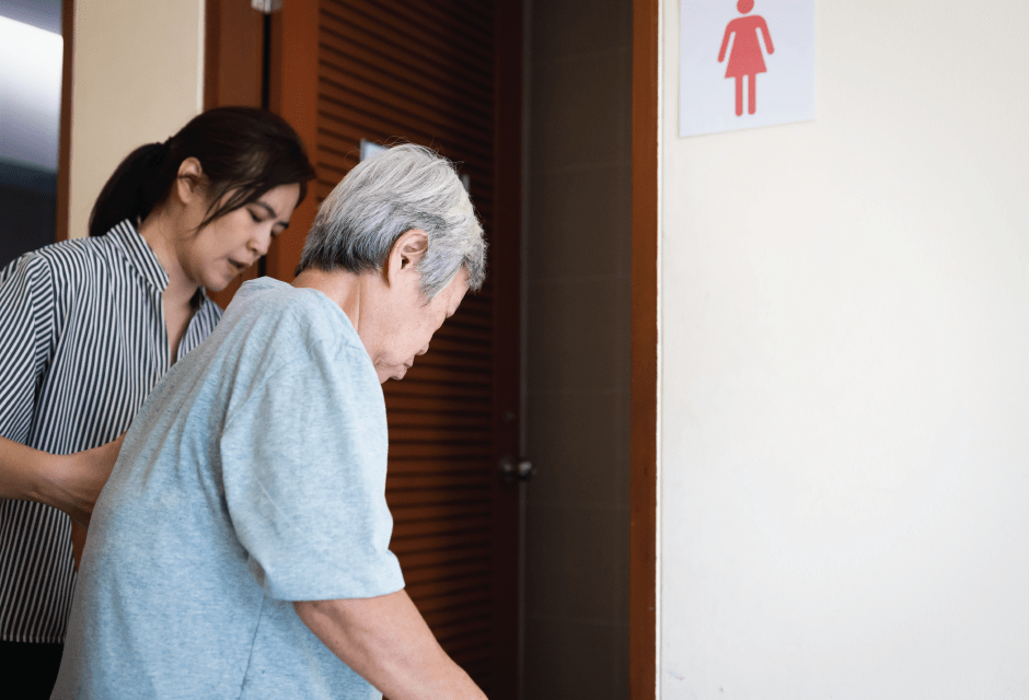 Elderly woman is being helped walk by caregiver.