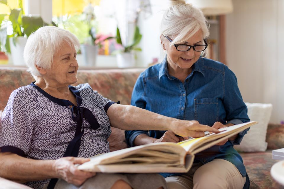 A senior woman and middle-aged woman look at photo album on the couch.
