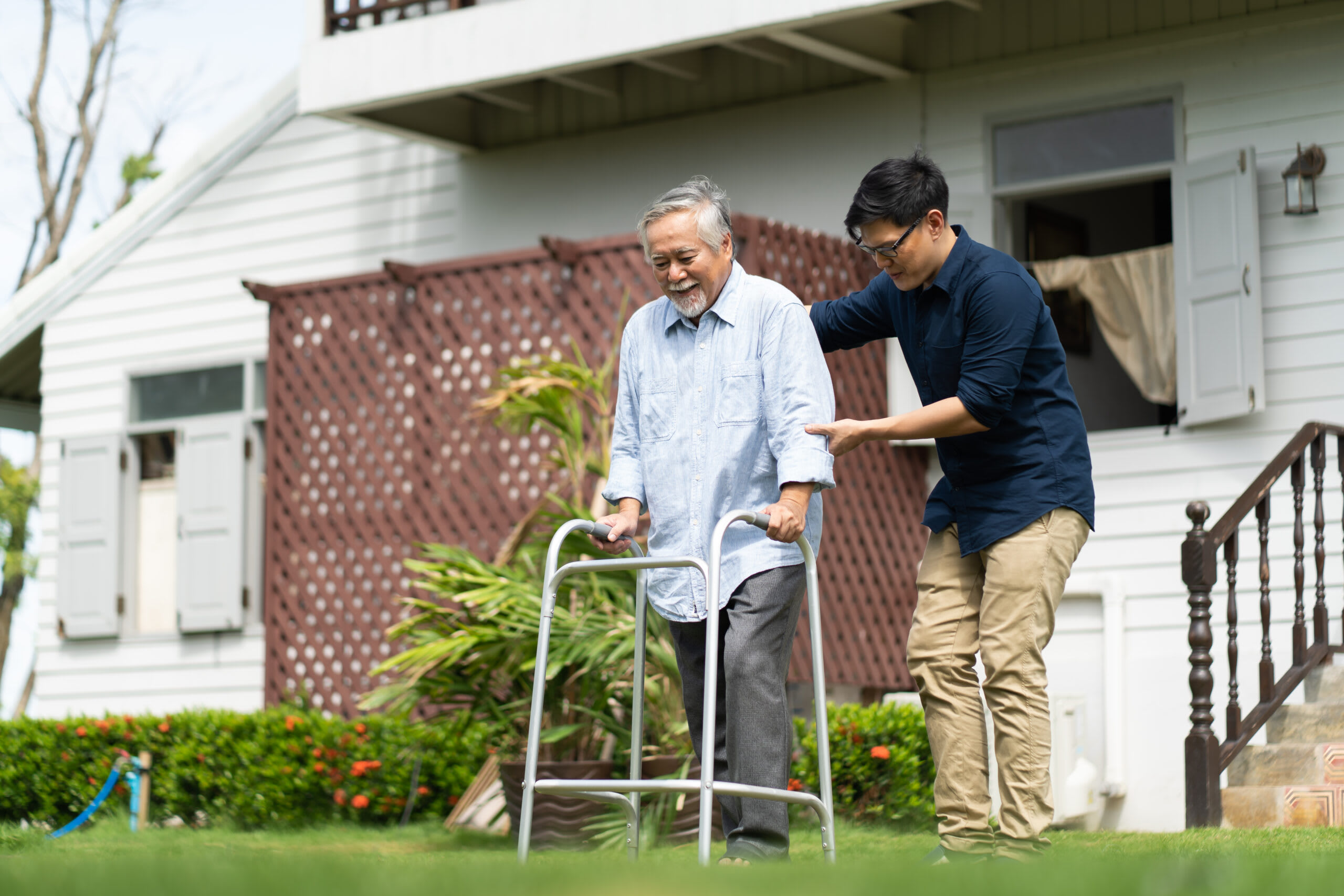 A man in glasses helps a senior man with a walker.