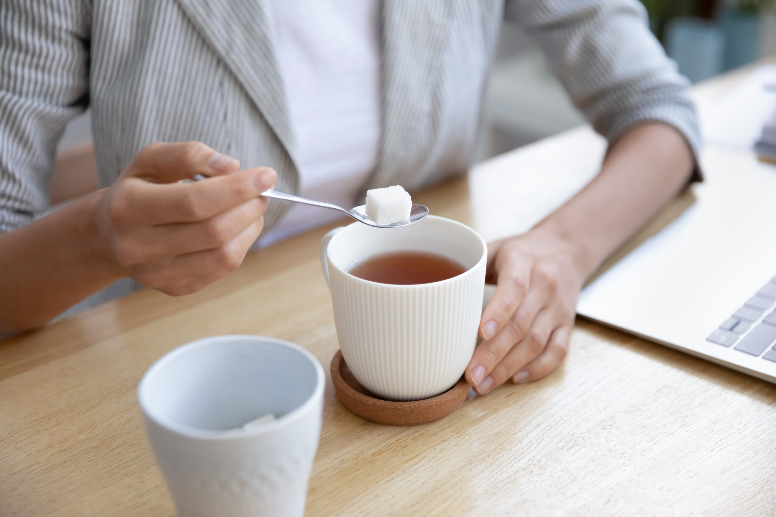 A senior woman stirs sugar in a cup of coffee.