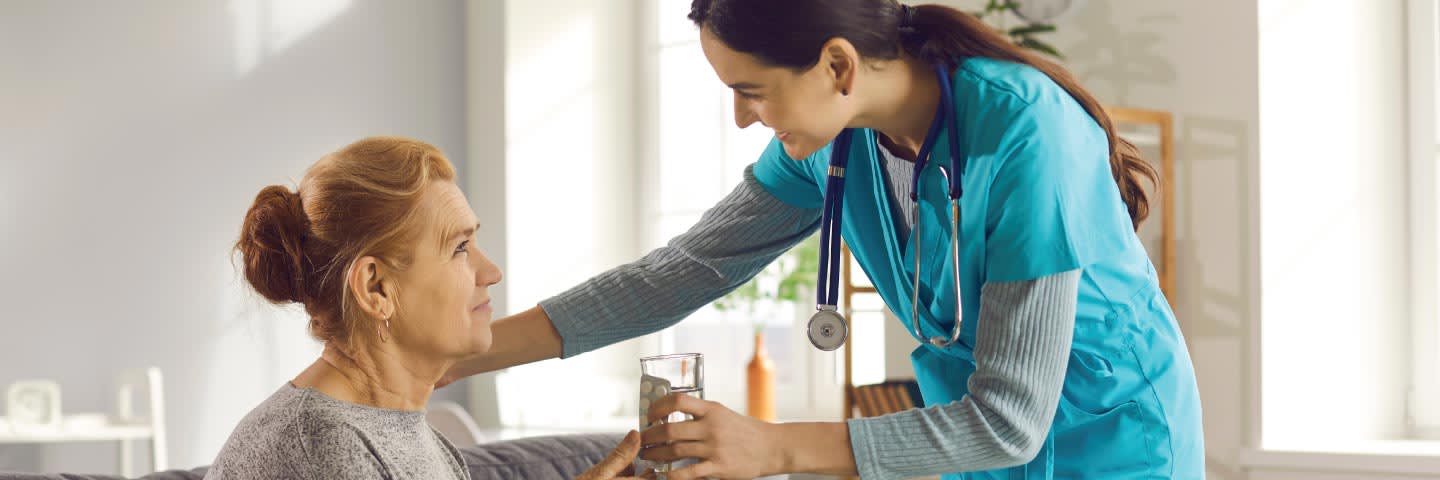 Nurse handing an elderly woman a glass of water