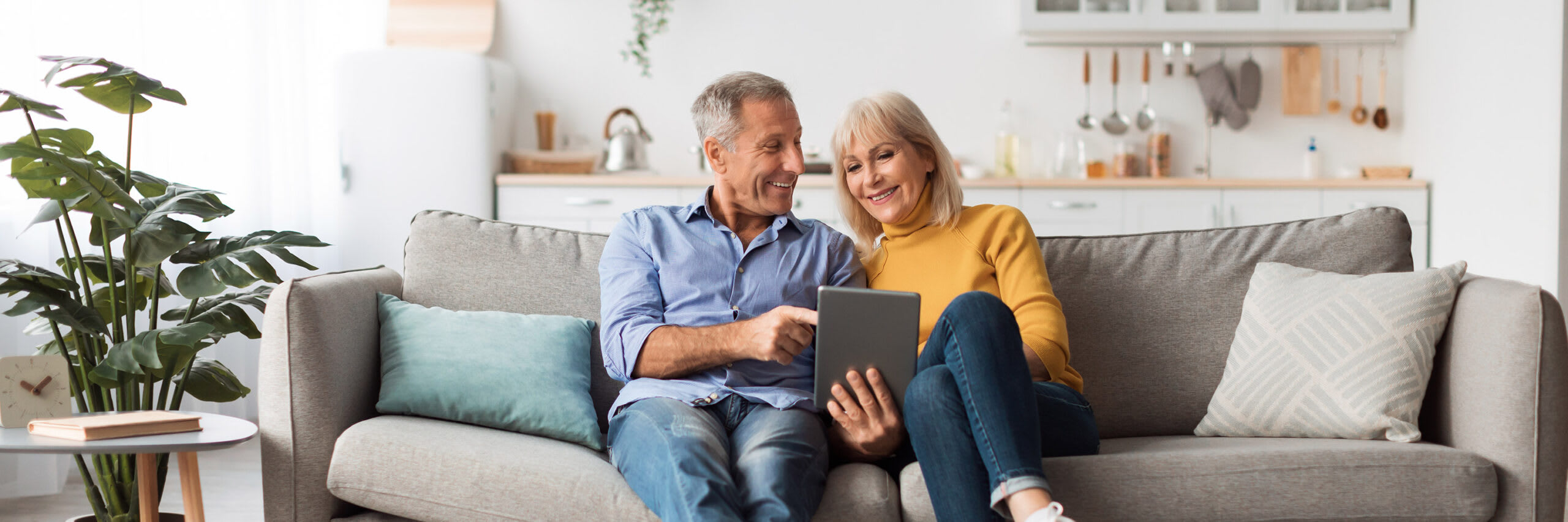 A senior couple sitting on a couch while reviewing information on a tablet