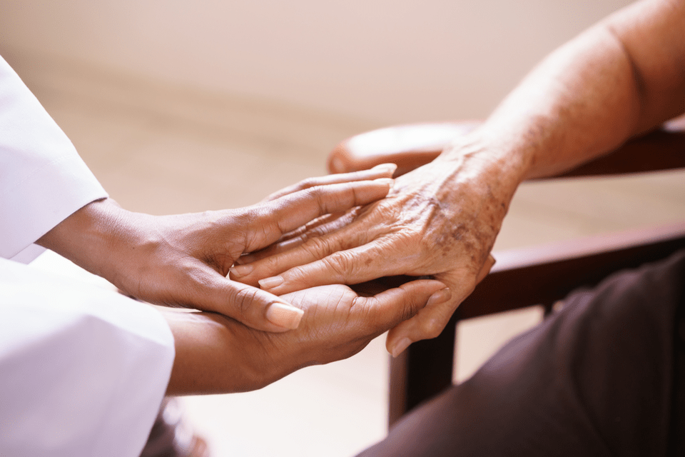 A young woman and senior hold hands while seated and discussing hospice care at senior living.