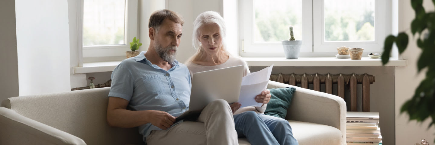 A senior couple sitting on a couch reviewing tax and assisted living forms