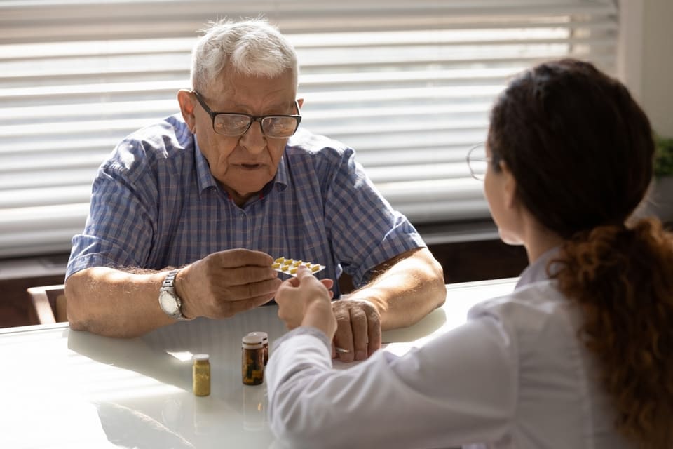 A senior man sits and chats with a doctor in an office.