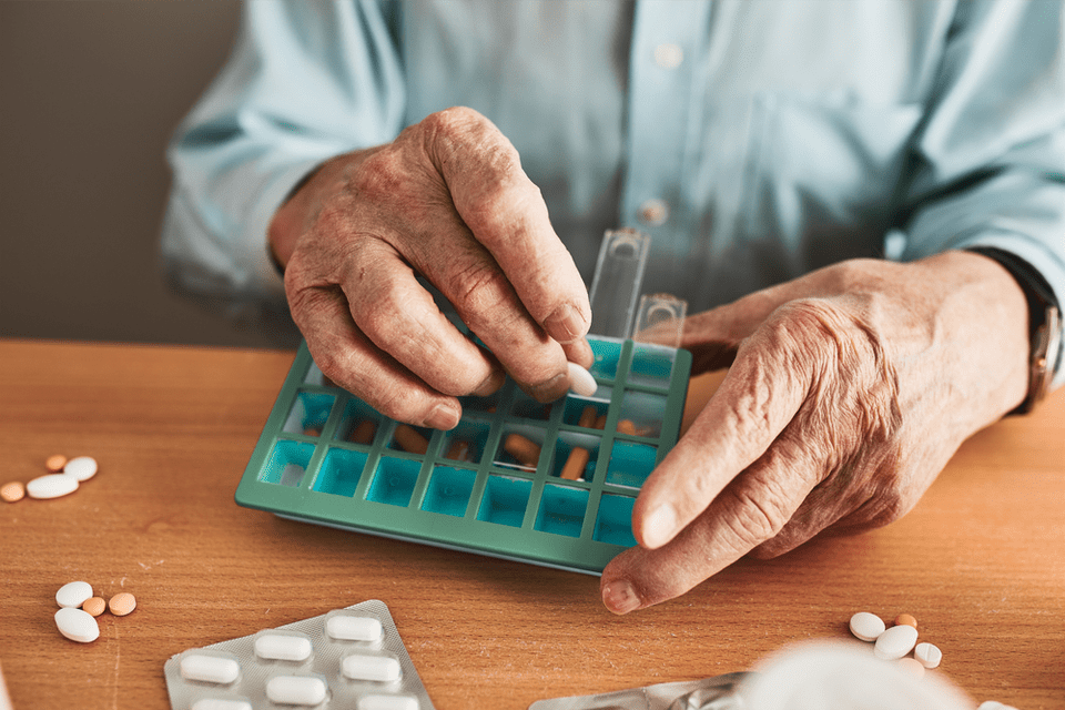 A senior man organizes pills into a container.