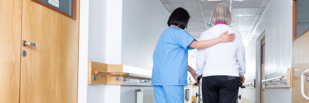 A nursing home caregiver helps a senior woman to use a walker