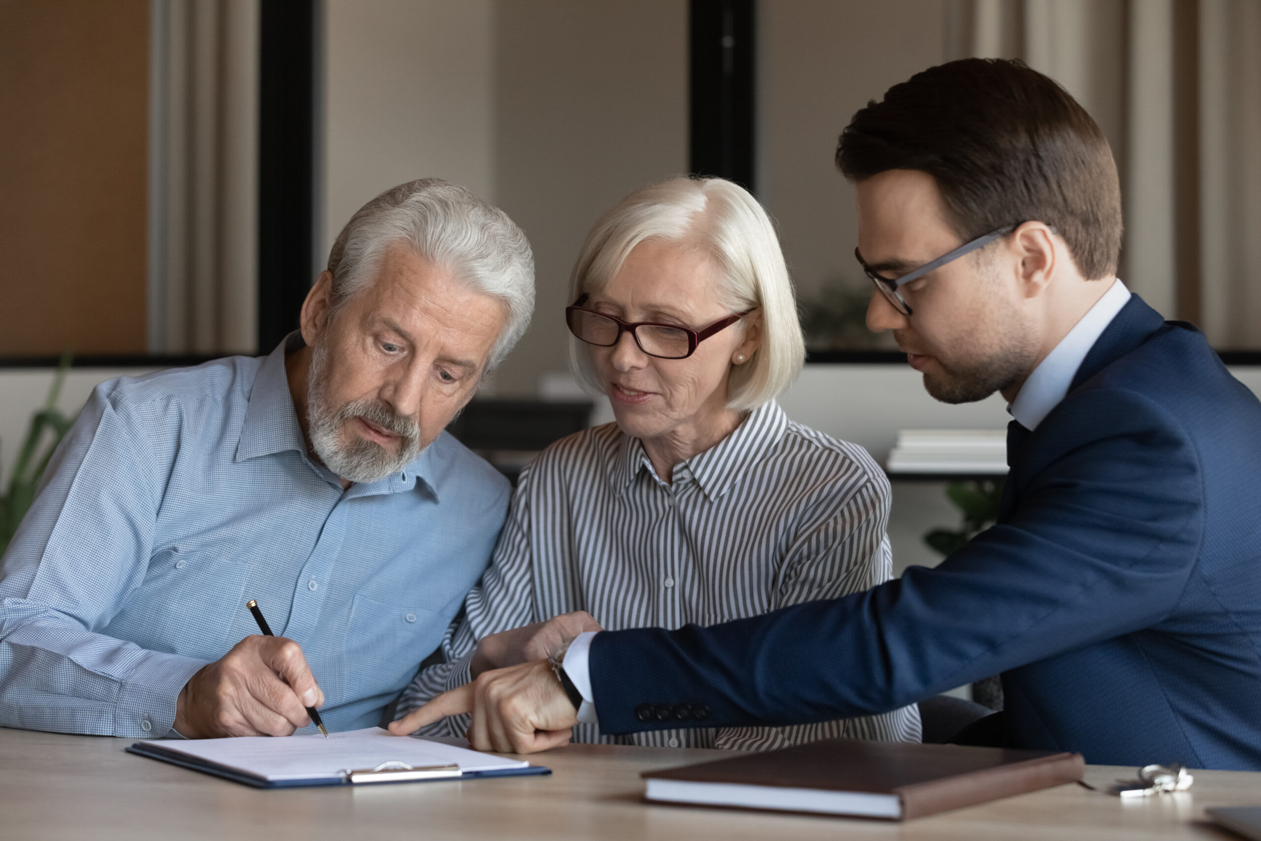 A man and senior woman sign papers in an office.