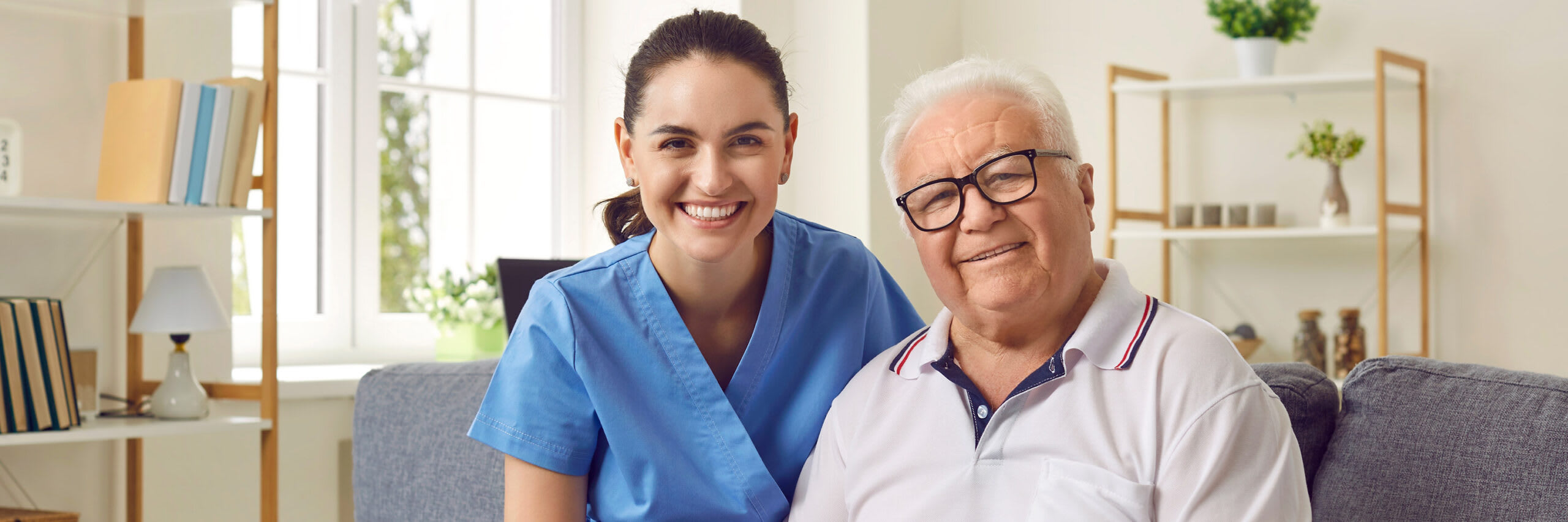 A caregiver and a senior smiling while sitting on a couch