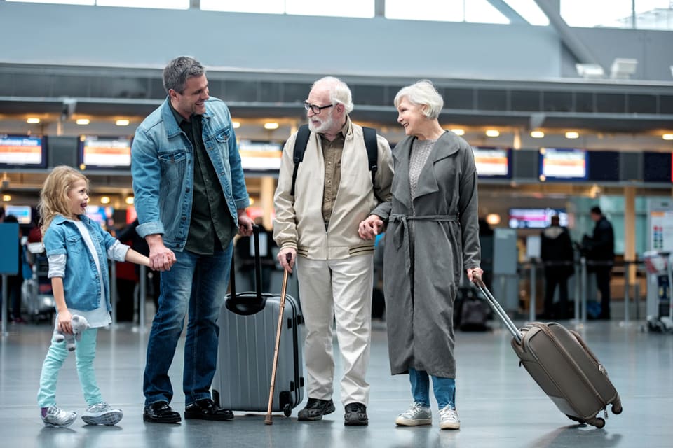 Two seniors and a man stand with a suitcase in an airport.