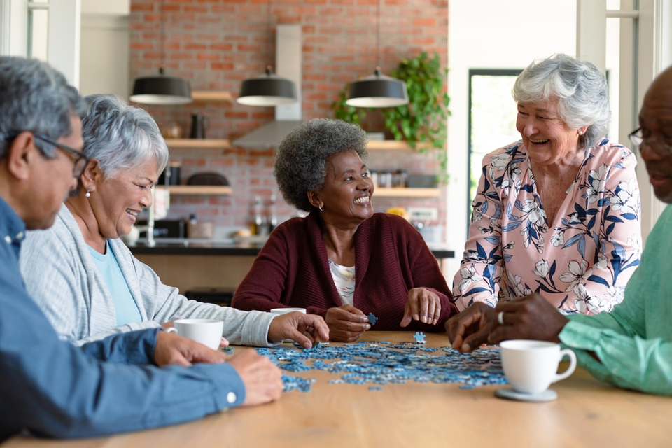 A group of seniors sitting around a table while socializing and putting together a puzzle