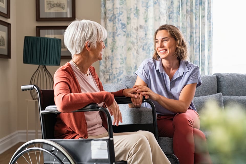 Woman holding talking to and holding of older woman in wheelchair