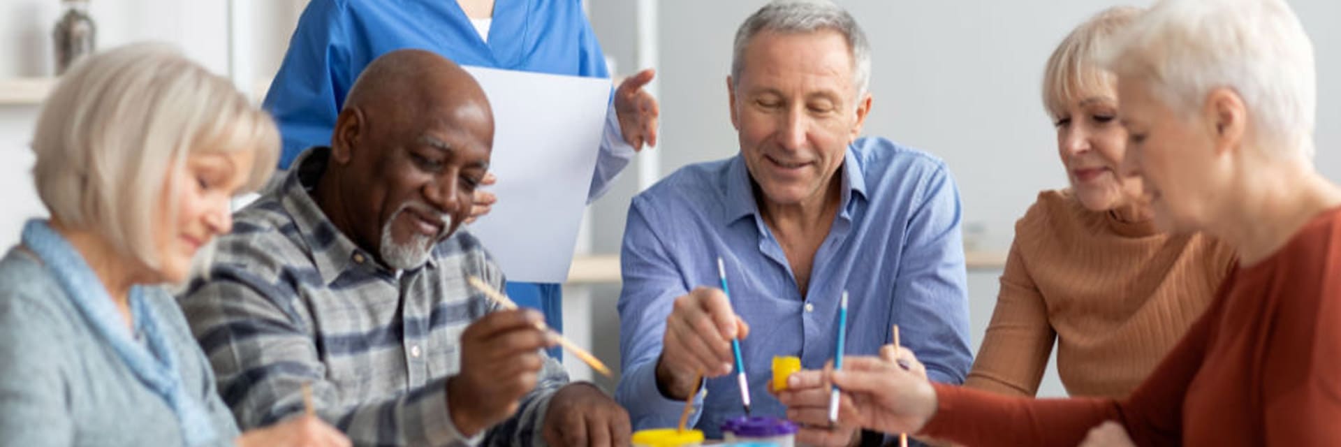 A staff member assists a group of seniors in an art program