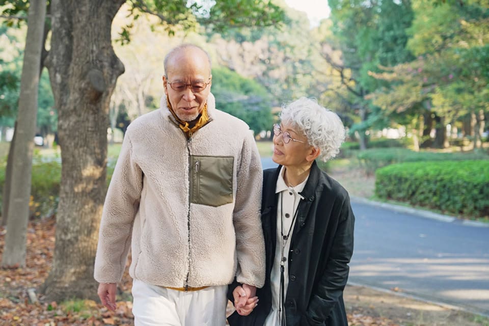 A senior man and woman walk through a park while holding hands.