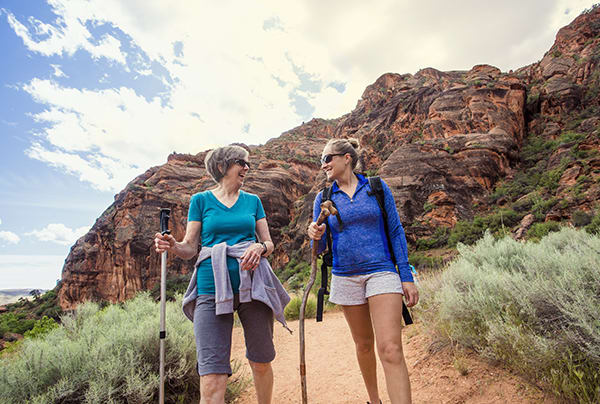 Two women talking while walking through the desert with walking sticks