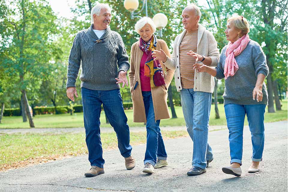 Two elderly couples walking in the park outside their independent living community