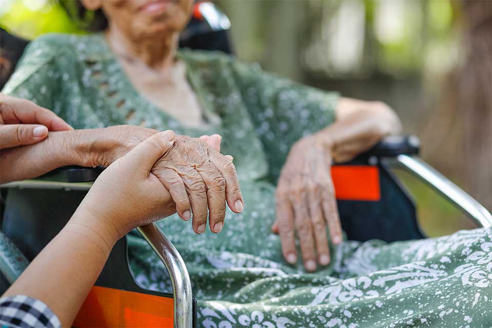 Elderly woman in wheelchair holding hands with her caregiver