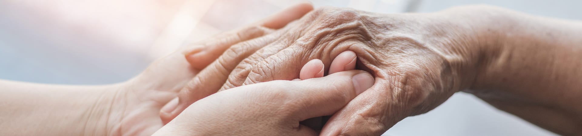 A closeup of a caregiver's hands holding a senior's hands in support