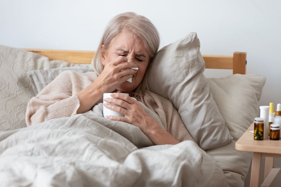 Sick older woman in bed with cup of tea and tissues
