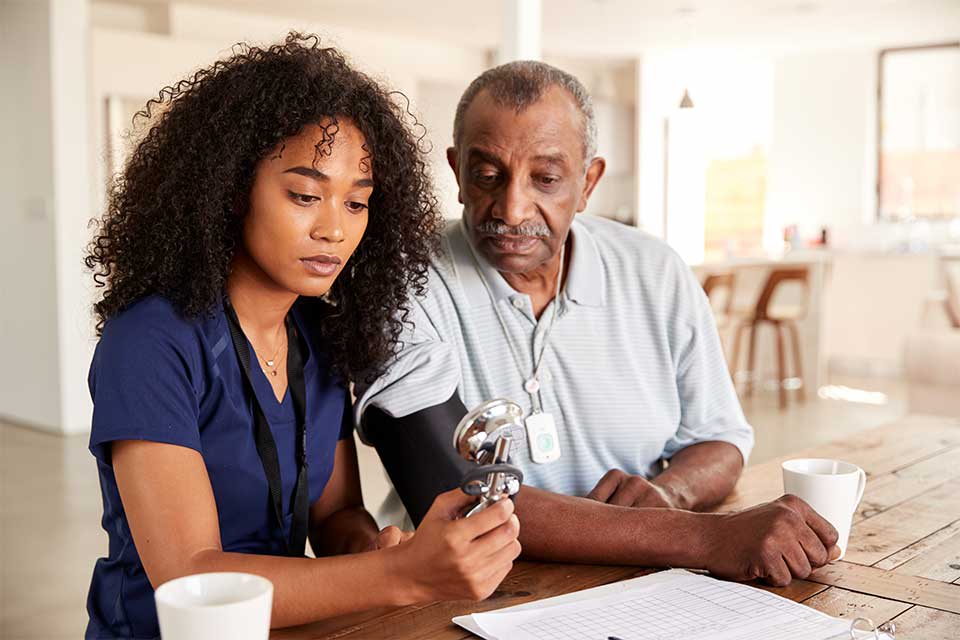 Female caregiver taking the blood pressure of elderly man.