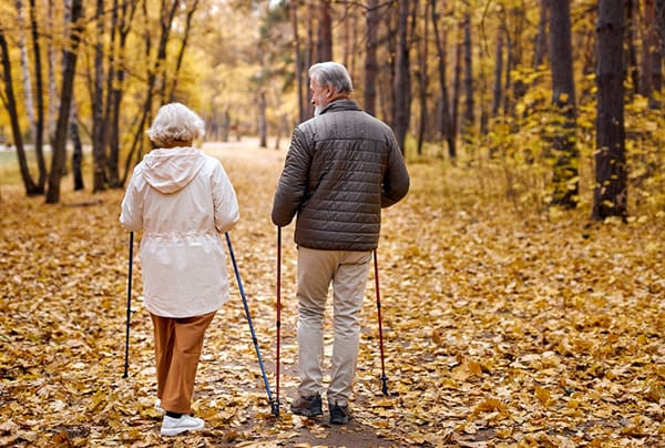 A senior couple walking through the woods during autumn while using walking poles