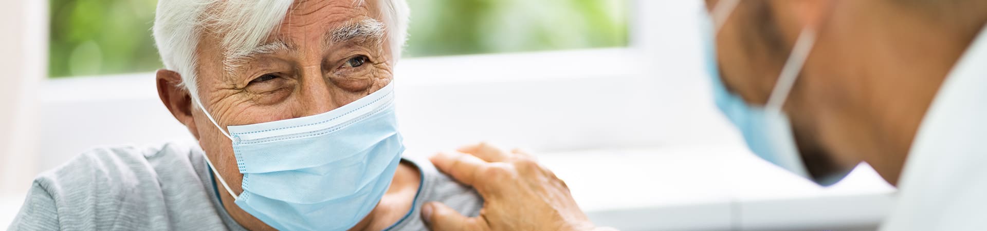 A doctor talking with a senior patient, both wearing medical masks